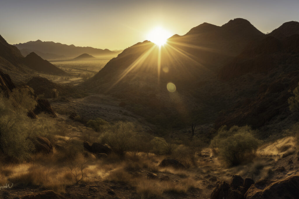 Embrace the mesmerizing spectacle of dawn breaking over the MacDonnell Ranges with this captivating image. The panoramic view frames the first light of day as it bathes the wilderness in golden sunlight, transforming the landscape into a living canvas. This is more than just an outdoor scene—it's a serene hymn to the awe-inspiring beauty of nature's daily rebirth. Begin your day with this stunning panorama, and let the tranquil beauty of the sunrise kindle your love for the grandeur of the Australian outback.