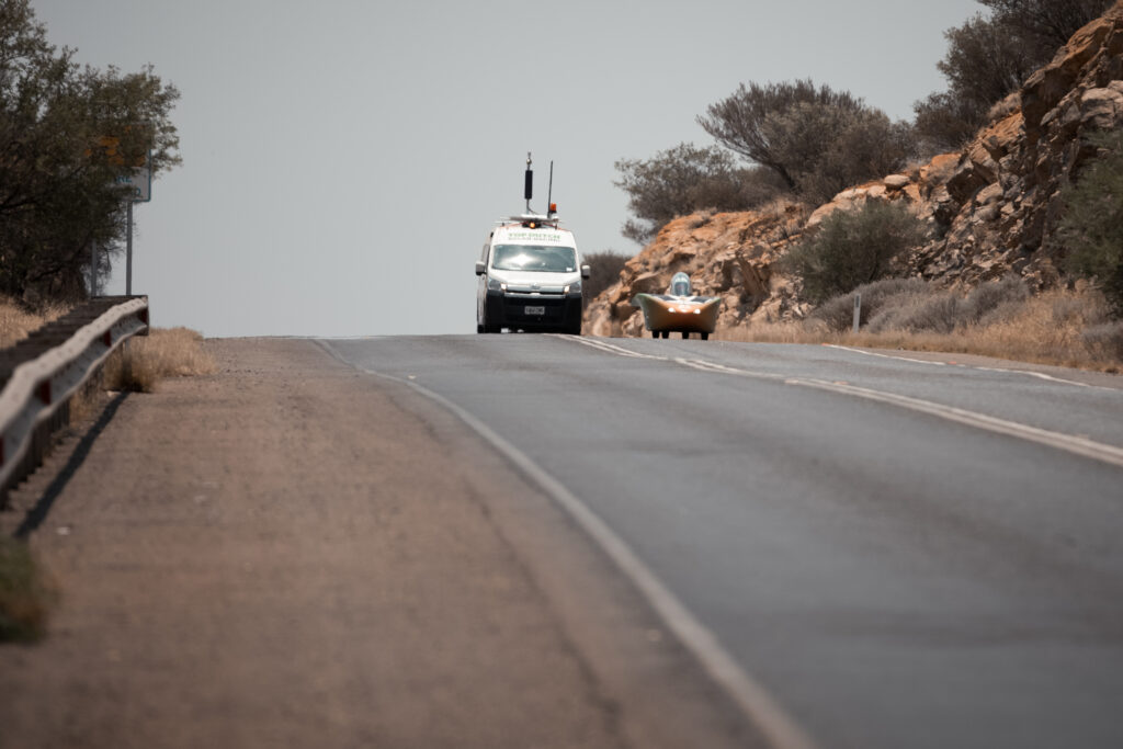 A captivating image showcasing a car on an open road, heading towards the grand event of Bridgestone World Solar Challenge 2023. The crisp view of the car, highway, and surrounding transportation amplifies the intense anticipation of this world-renowned event. Visit worldsolarchallenge.org for more info.