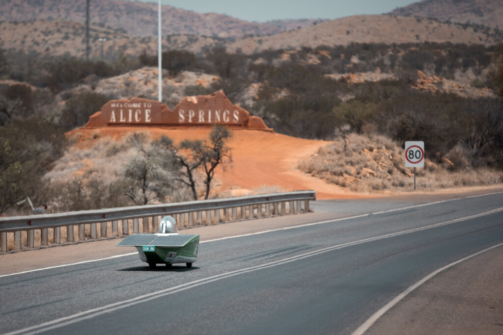 An immersive picture capturing the expansive highway leading to the vibrant city of Alice Springs. Captured in the frame is a lone person, embodying the spirit of excitement for the upcoming 2023 Bridgestone World Solar Challenge. Welcome to an adventure powered by the sun, encapsulated in one beautiful image.