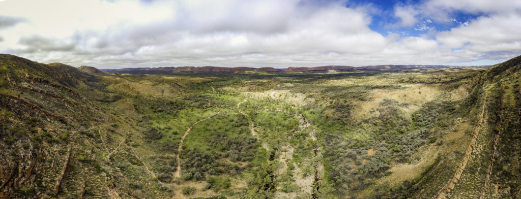 This breathtaking aerial snapshot captures the serene aftermath of nature's fury, showcasing the resilience of the Northern Territory landscape. As the river asserts its path through Serpentine Gorge, it creates a contrast with the surrounding woodland and lush vegetation that have weathered the storm. The sky, clear and untroubled, watches over the scene, a testament to the undisturbed beauty of the outdoors. Witness the wonder as the wilderness bounces back, revealing a tapestry of natural splendor and scenic vistas stretching out into the horizon.